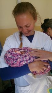 Ingrid med en baby tullet inn i teppet som hun har strikket.